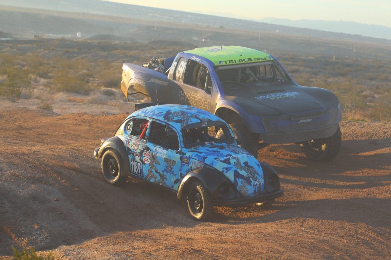 A VW Bettle races beside a Trophy Truck.