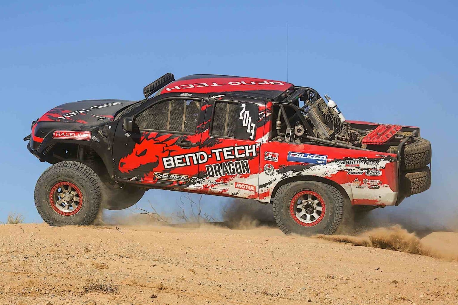 A racing truck jumping over a dirt dune.
