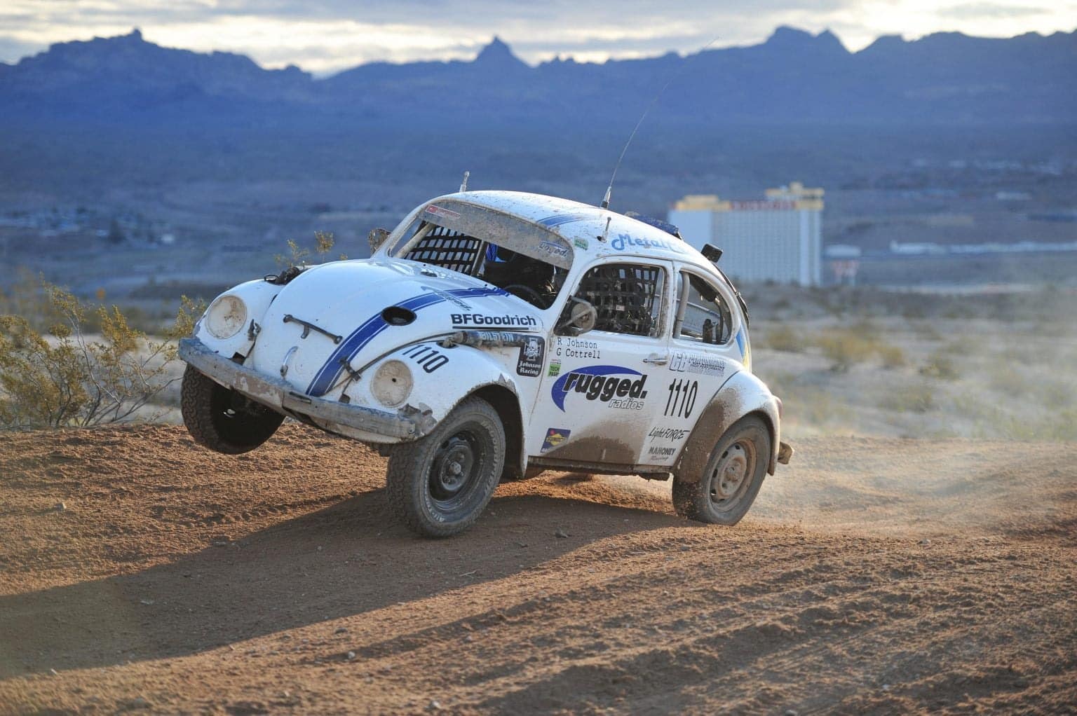 A VW Bettle racing on a dirt track and leaping through the air.