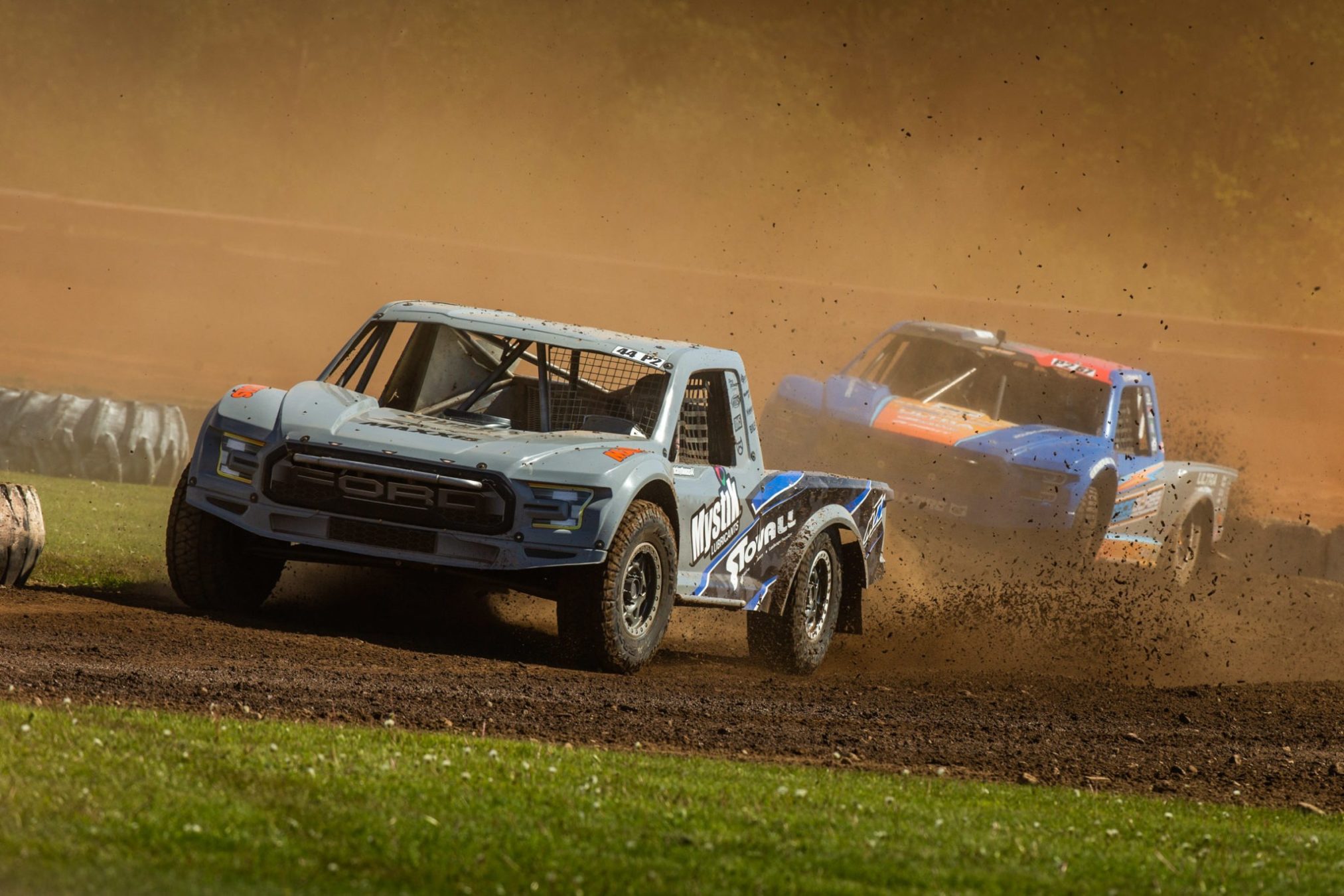 Two racing trucks racing on the dirt race road.